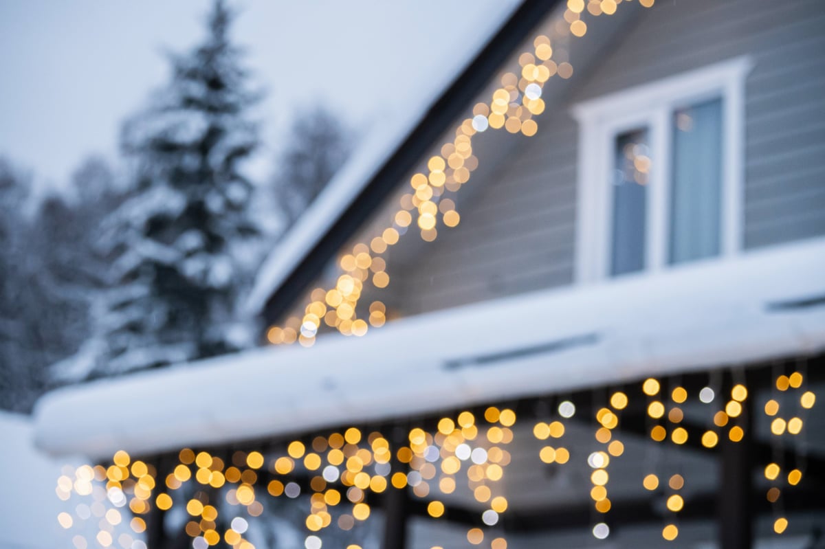 Snowy winter house in forest with bokeh of festive Christmas lights creating a dreamy holiday atmosphere