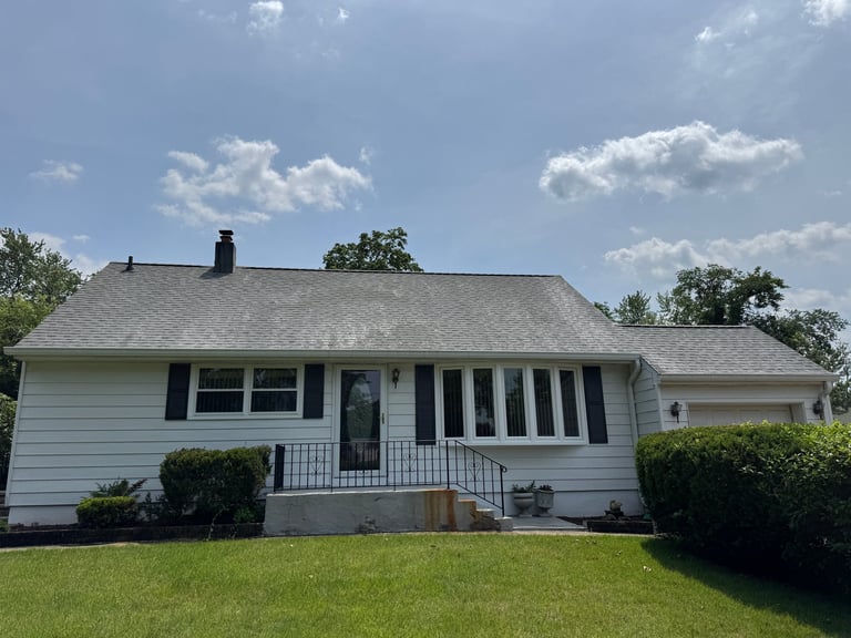 White ranch-style house with covered porch, gray roof, and landscaped front yard on a sunny day