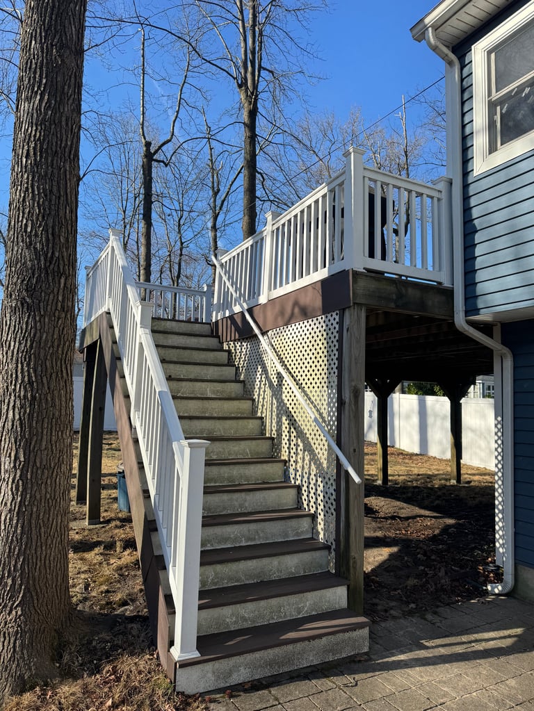 Exterior wooden stairs with white railings leading to an elevated residential deck attached to a blue siding house