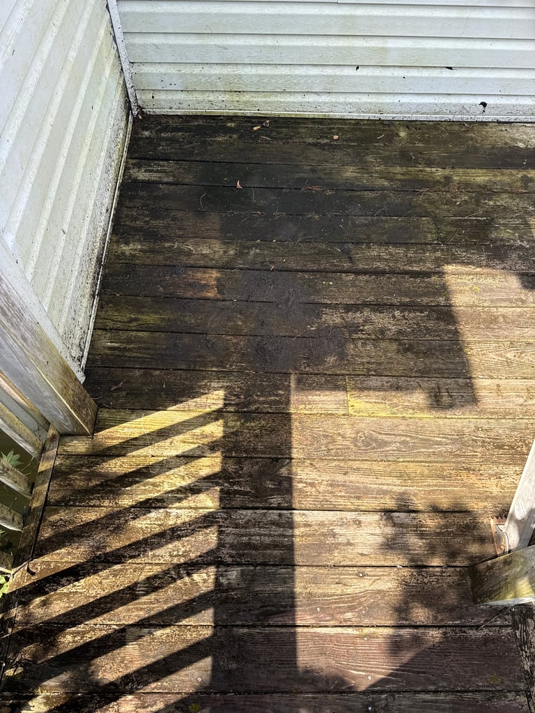Wooden deck with railings casting shadows, showing varying stain colors and wear patterns