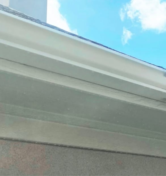 Close-up of white gutter and soffit on a house exterior against clear blue sky with clouds